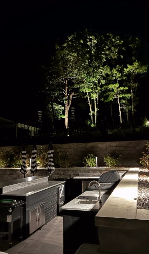 Outdoor kitchen with uplit trees in the background at night