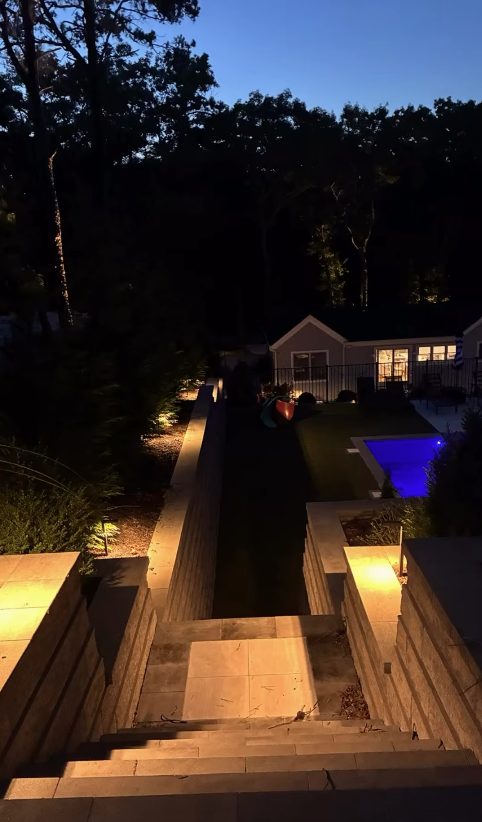 Lit steps leading down to a pool and patio at night